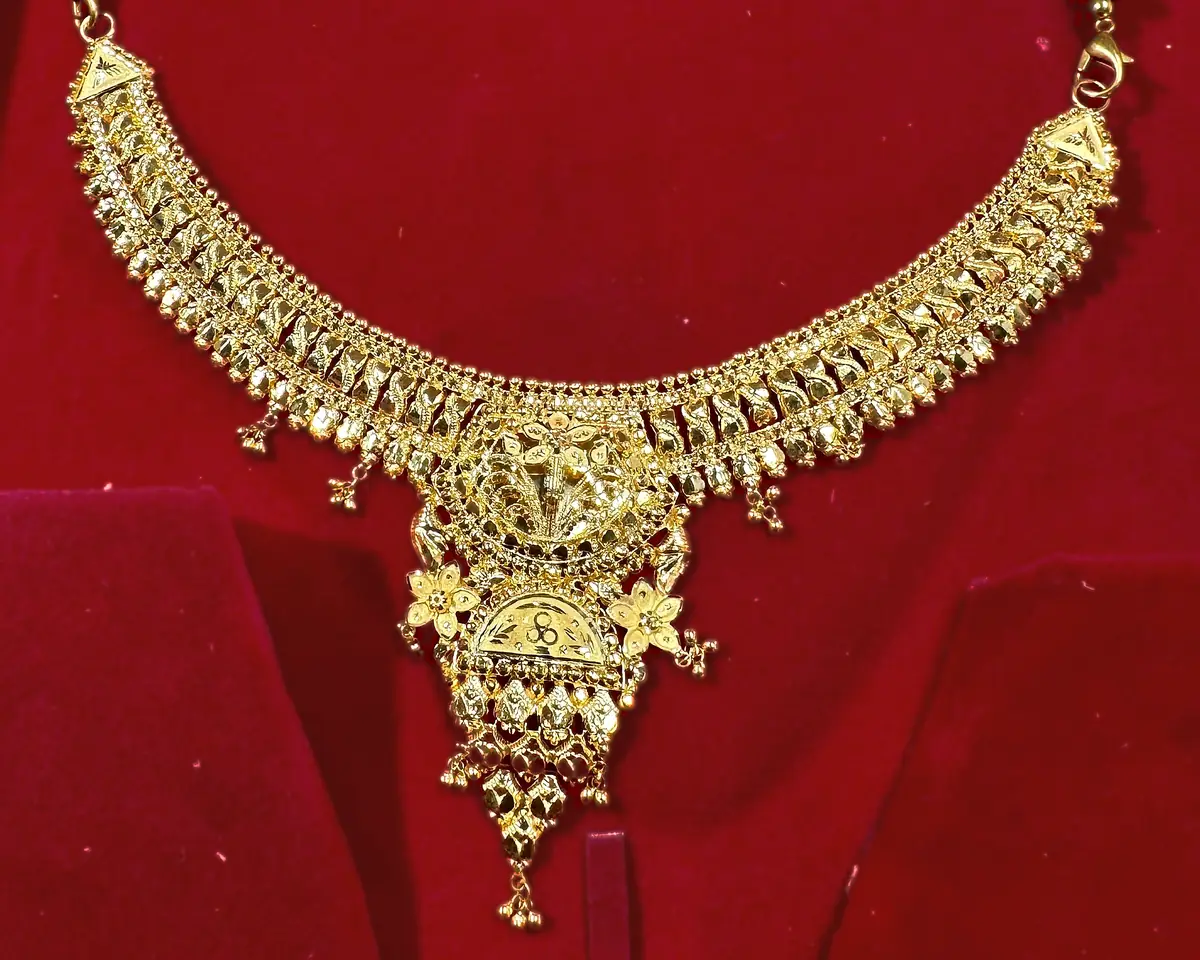 The same gold necklace in its red velvet box, seen wider. The velvet covers about four fifths of the picture and there is no white or grey anywhere in the frame to balance the colour against.