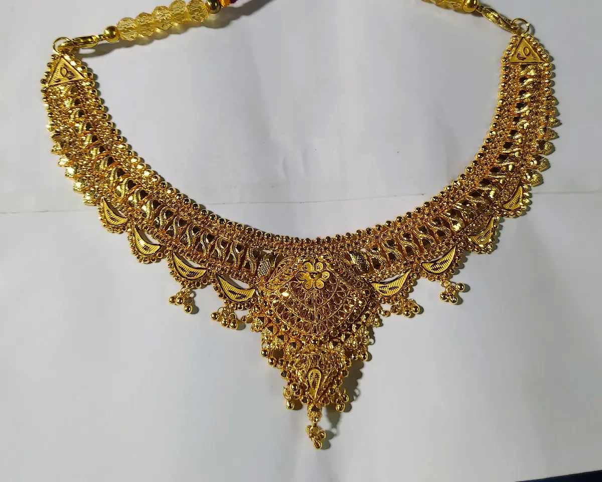 A gold necklace laid on a plain sheet of white paper on the shop counter. The paper fills most of the frame and gives the camera something known to be neutral to balance the colour against.